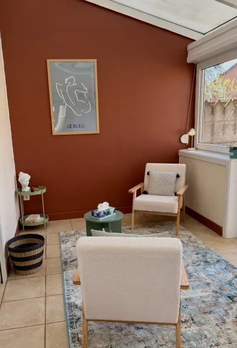Cabinet de psychologue à la décoration chaleureuse avec fauteuils clairs, mur terracotta, lumière naturelle et ambiance apaisante.
